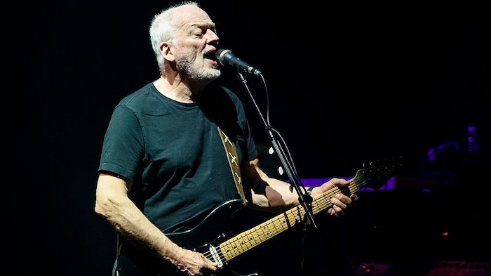 David Gilmour chante et joue de la guitare sur scène.