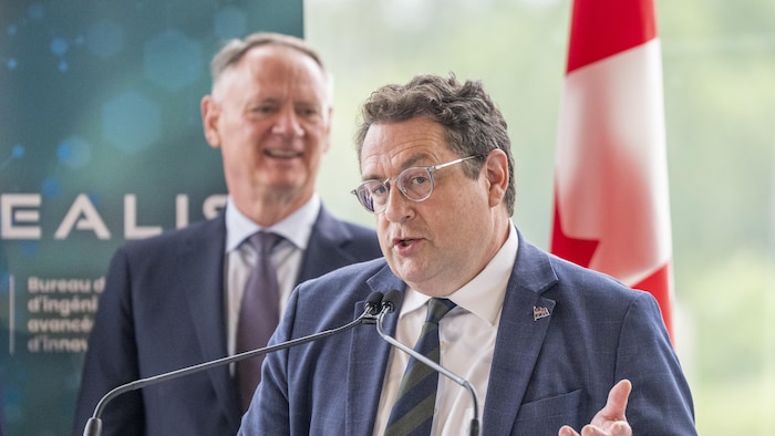 Bernard Drainville parle, avec derrière lui David McGuinty.