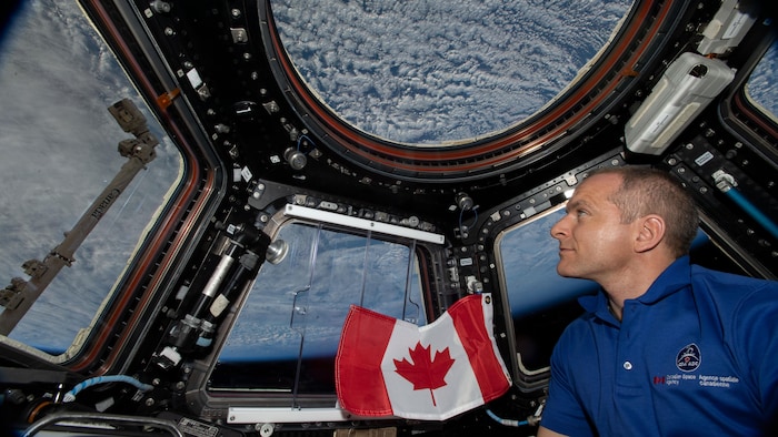 Il regarde la Terre par une fenêtre de la Station spatiale internationale.