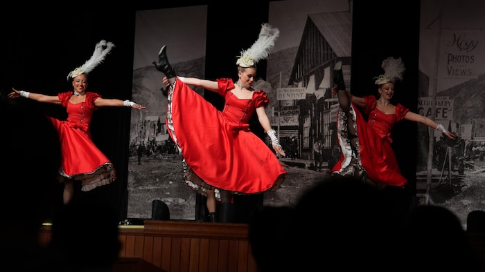 Trois jeunes femmes en robe rouge dansent sur une scène à Dawson, le 10 mai 2024. 