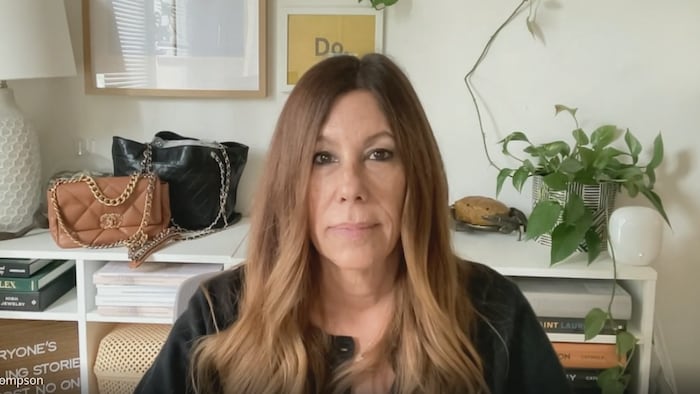 Une femme prend la pose devant une bibliothèque sur laquelle reposent deux sacs de luxe. 