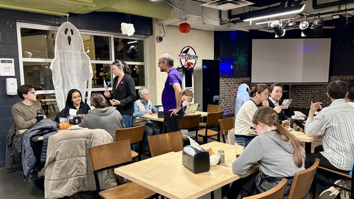 Amir Zuccolo, candidate à la mairie de Charlottetown, est debout. Elle discute avec trois étudiants assis à une table.