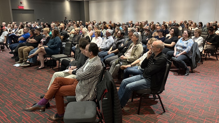 Une salle est remplie de personnes assises et attentives.