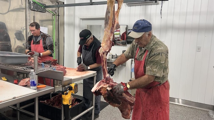 Trois hommes coupent de la viande dans un bâtiment.