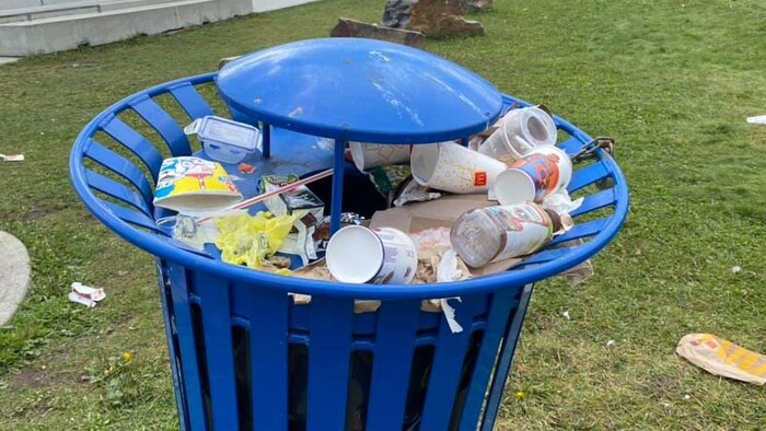 Une poubelle publique déborde de déchets.