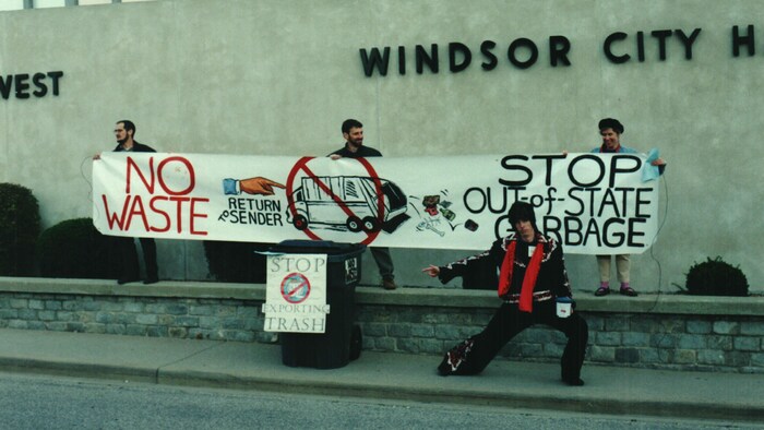 Trois hommes tiennent une pancarte demandant l'arrêt de l'exportation de déchets de Toronto vers le Michigan.