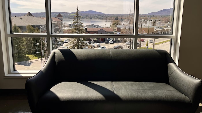 Un sofa devant une grande fenêtre ouvrant sur un lac et une montagne. 