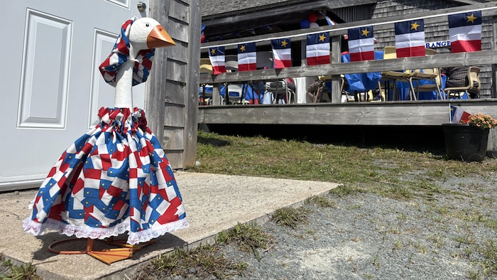Une oie sculptée devant une porte est décorée avec une jupe aux couleurs du drapeau acadien et un petit ruban.