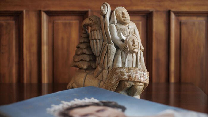 Un livre avec le portrait de la reine Elizabeth et une figurine autochtone.