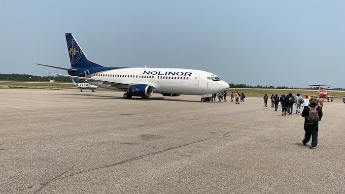 Des résidents marchent sur le tarmac, vers un avion.