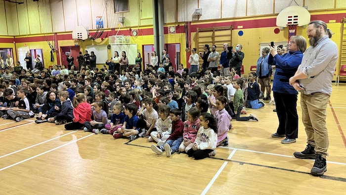 Des enfants sont assis dans un gymnase.