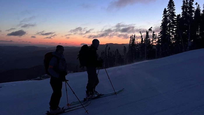 Deux skieurs en ascension devant un paysage crépusculaire.