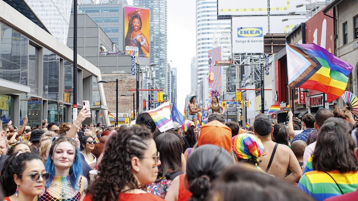 Des personnes portant des vêtements célébrant la Fierté LGBTQ marchent dans une rue achalandée.