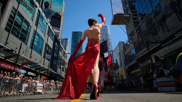 Une drag queen en robe rouge défile devant les spectateurs.