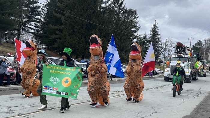 Des citoyens déguisés en dinosaures défilent dans la rue.