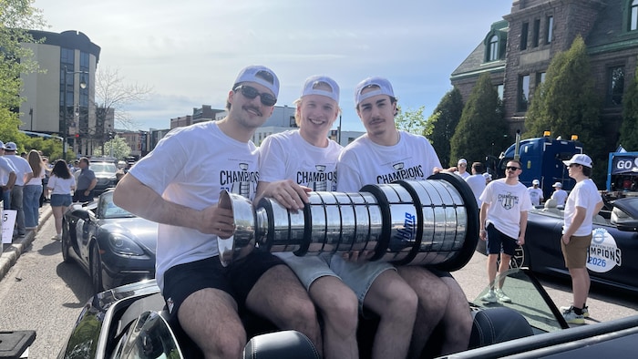 Trois personnes tiennent un trophée à l'arrière d'une voiture.