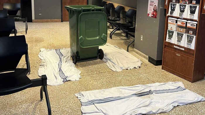 Une poubelle au milieu d'une salle d'attente. Plusieurs serviettes sont étendues au sol. 
