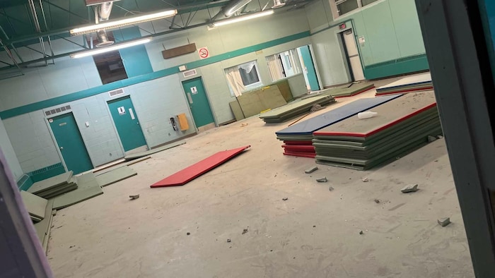 Dans une grande salle éclairée par des fluorescents, des morceaux de béton jonchent le sol, sali. Les vitres d'un bureau situé tout au fond de la salle sont cassées.