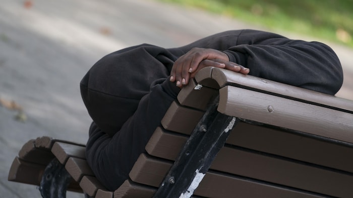 Un homme afro-américain est couché sur un banc de parc.