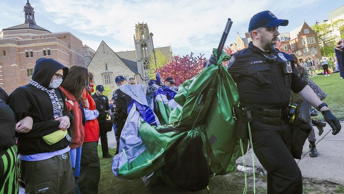 Un agent tire une tente devant des manifestants. 