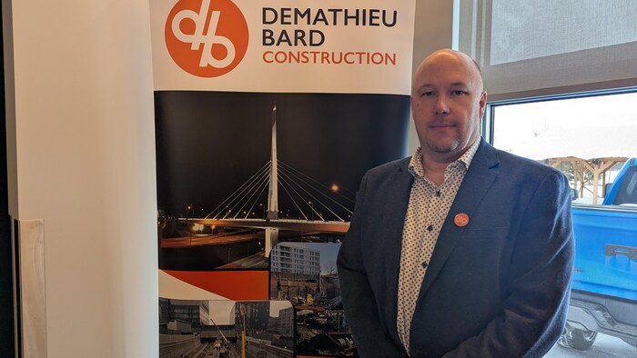 Steve Cloutier pose devant une affiche de l'entreprise. 