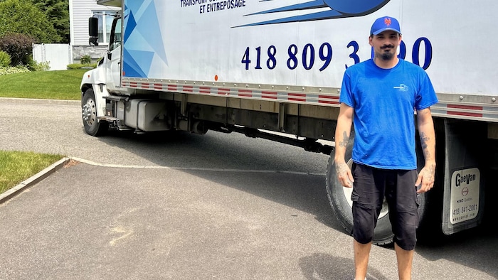 Un homme pose devant un camion de déménagement.