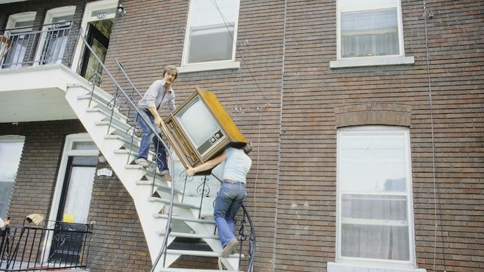 Deux hommes transportent un téléviseur dans les escaliers d'un immeuble à logement.