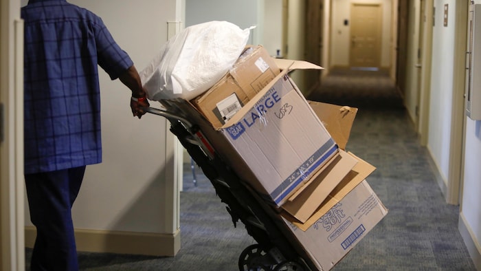 Un homme tire une pile de boîtes de carton vides empilées dans le corridor d'un immeuble à appartements.