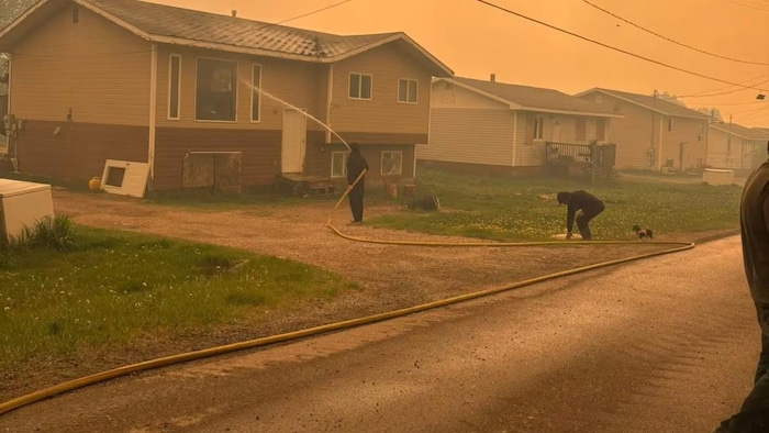 Deux personnes nettoient au tuyau d'arrosage les maisons de la communauté autochtone de Denare Beach.