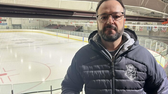 Un homme avec manteau noir, debout devant une glace 