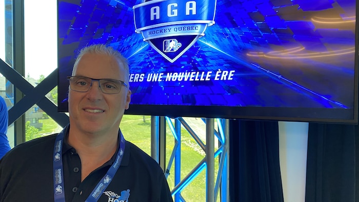 Denis Dumaresq devant un écran qui présente l'assemblée annuelle de Hockey Québec.