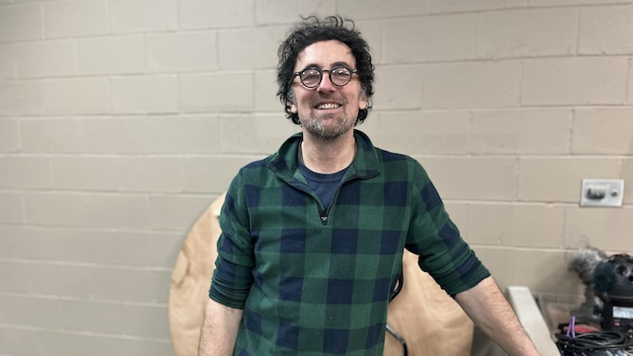 Un homme en chemise verte carreautée est debout dans son atelier, une main posée sur l'établi.