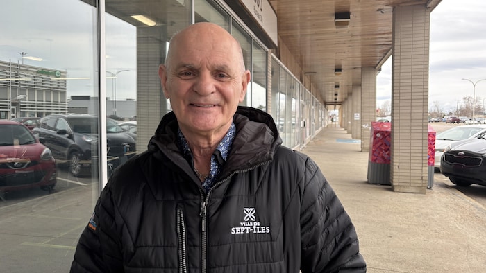 Denis Miousse sourit à la caméra, dehors, à côté d'un bâtiment vitré.