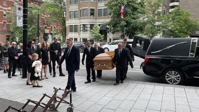 Quatre hommes transportent un cercueil près d'un corbillard.