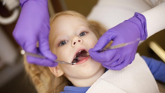 طبيب أسنان (لا نرى وجه أو وجهها) يعاين طفلاً.