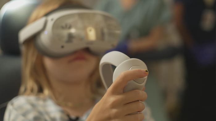 L'enfant est équipée d'un casque de réalité virtuelle et d'une manette.