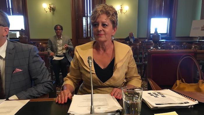 Katherine d'Entremont, assise à une table, s'apprête à lire son rapport à l'Assemblée législative
