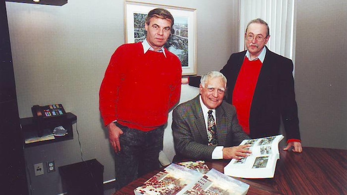 Three men smile for a photo with a big book in his hands.