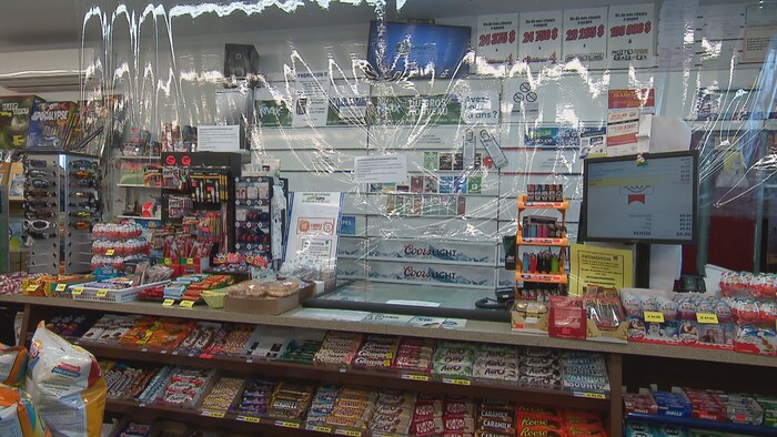 Un voile de plastique entoure la caisse de ce dépanneur pour protéger les employés contre la propagation du coronavirus.