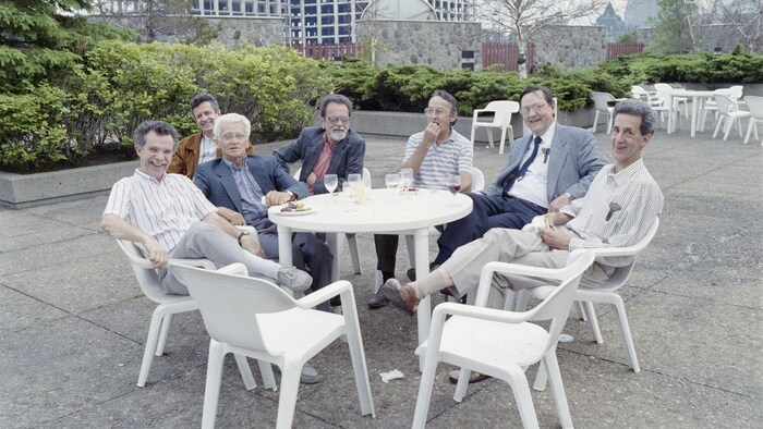 Sur la terrasse de la Maison de Radio-Canada, sept hommes sont rassemblés à une table pour célébrer leur départ à la retraite.
