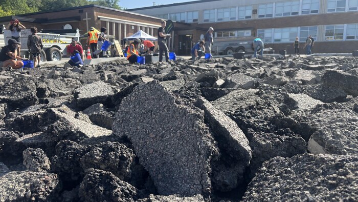 Gros plan sur des morceaux d'asphalte concassés avec des personnes qui les ramassent en arrière-plan.