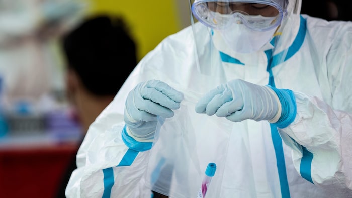 Un travailleur de la santé couvert d'équipement de protection met un échantillon dans un sac à Samut Sakhon, en Thaïlande.