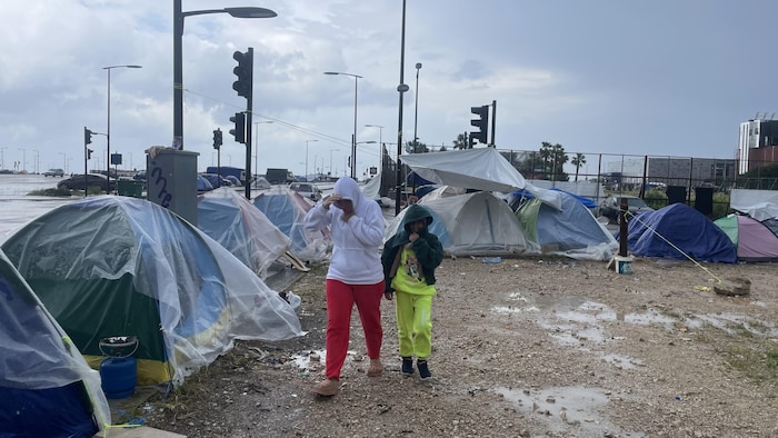 Une femme et sa fille marchent sous la pluie vers leur tente.