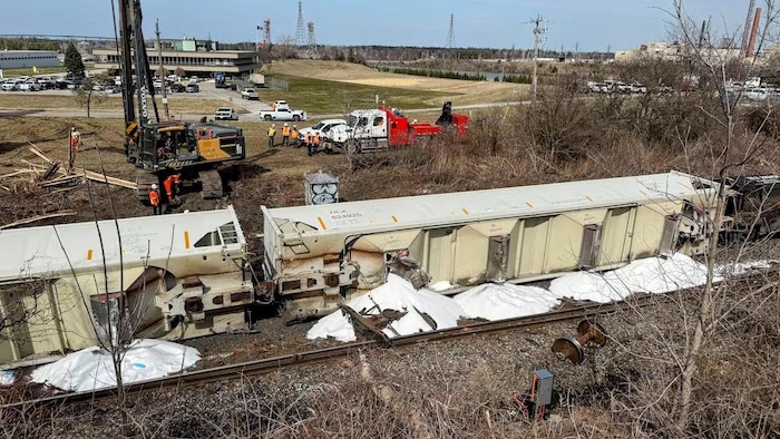 Une substance blanche et granuleuse se déverse de deux wagons alors qu’une crue est sur place pour dégager les rails.