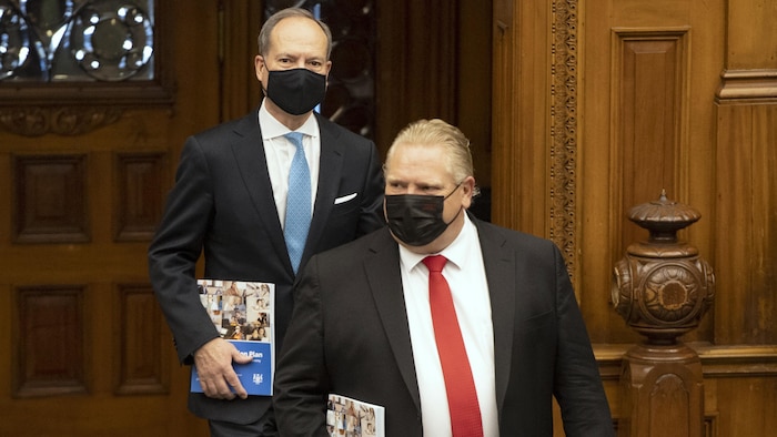 Deux hommes portant un masque noir entrent dans une salle.