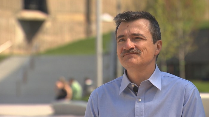 Un homme portant la moustache et souriant en entrevue à l'extérieur de l'Université de Montréal.