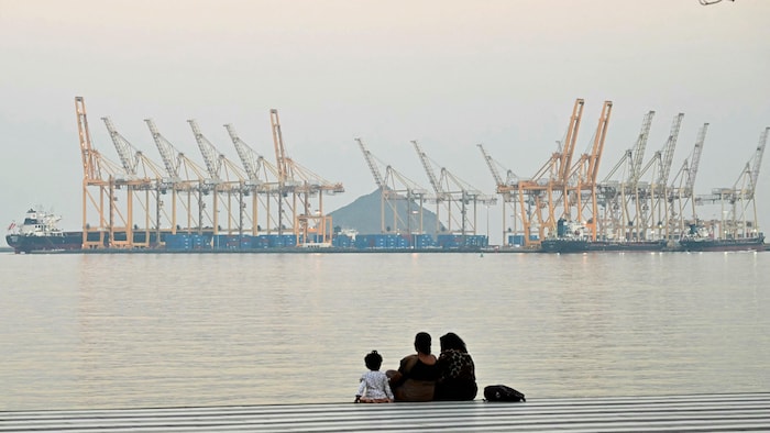 Une famille, assise sur le bord de l'eau, regarde au loin le chantier naval.