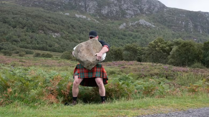 Un homme soulève une très grosse pierre. 