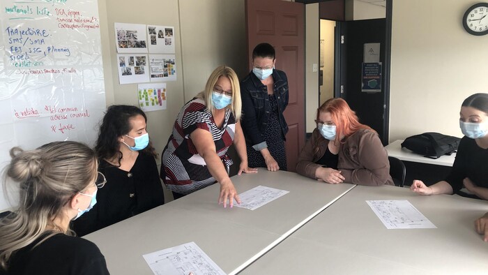 Un groupe de femmes regarde les plans du local sur une feuille au centre d'une table.