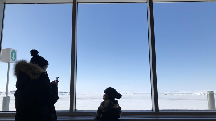 À l'aéroport de Puvirnituq, une femme et son enfant, silhouettes en contre-jour, regardent la piste d'atterrissage.